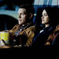 a man and a woman are sitting in a car with a yellow bucket of popcorn