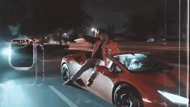 a man in a red jacket is sitting on the back of a red sports car .
