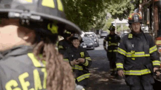 a group of firefighters are walking down a street in front of a fire truck