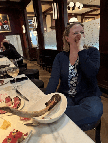 a woman is sitting at a table with a plate of food and a steak on it