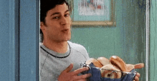 a man is holding a bowl of hot dogs and bread .
