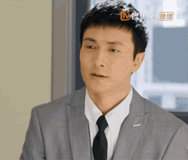 a man in a suit and tie looks at the camera with a tv advertisement in the corner