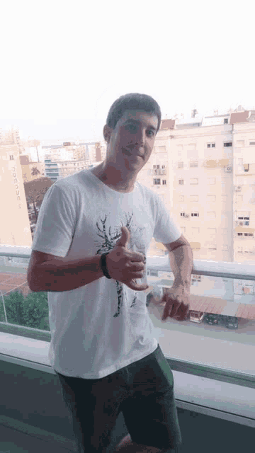 a man wearing a white shirt with a deer on it is standing on a balcony
