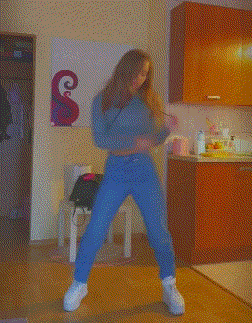 a woman is dancing in a kitchen with a painting of a cat on the wall behind her