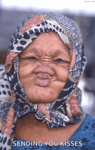 an elderly woman wearing a scarf around her head is making a funny face and sending you kisses .