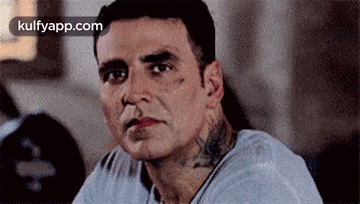a man with a tattoo on his neck is sitting down and looking at the camera .