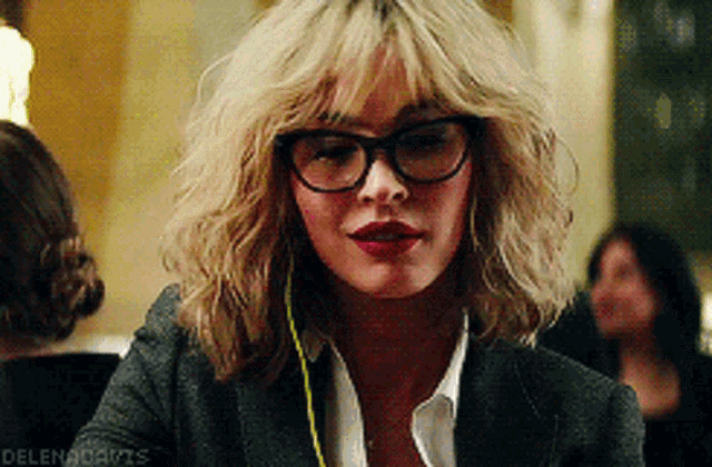 a close up of a woman wearing glasses and a gray jacket