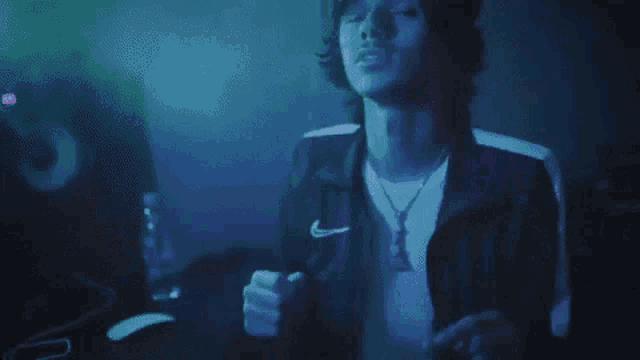 a man in a nike jacket is dancing in a dark room with a blue light behind him .