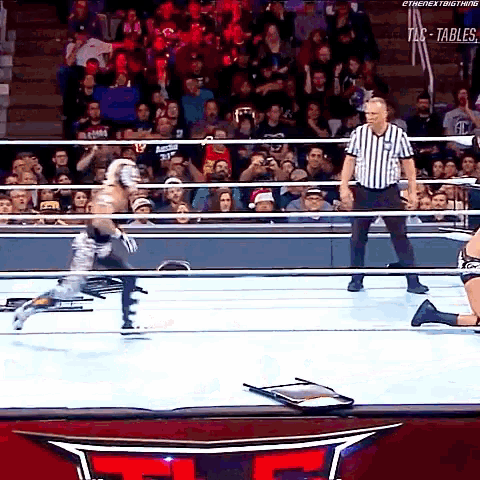 a referee stands in a wrestling ring while a wrestler is kneeling down