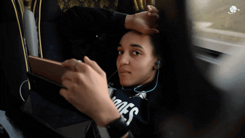 a woman wearing headphones and a hoodie that says moes is looking at her phone