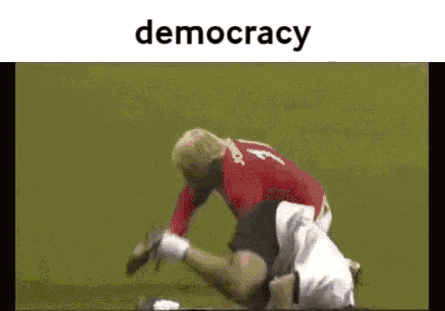 a soccer player in a red shirt is being tackled by another player on a field .