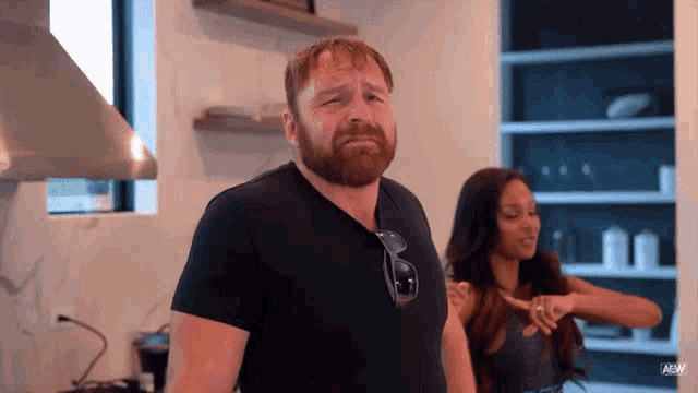 a man with a beard wearing sunglasses stands next to a woman in a kitchen ..