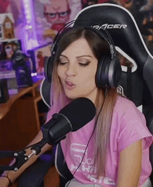 a woman wearing headphones and a pink shirt is singing into a microphone while sitting in a chair .