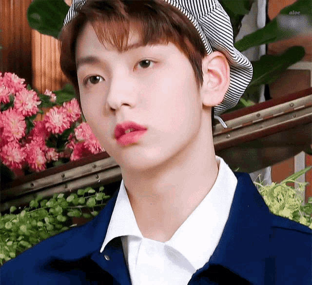 a young boy wearing a hat and a blue jacket is standing in front of flowers .
