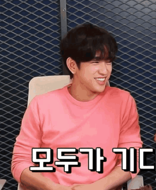 a man in a pink shirt is smiling in front of a metal mesh wall