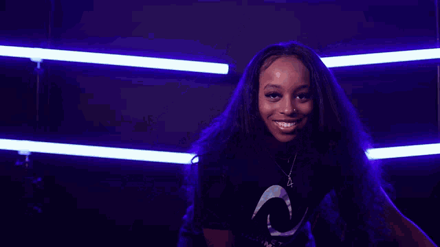 a woman wearing a black t-shirt with a crescent moon on it is smiling in front of purple lights .