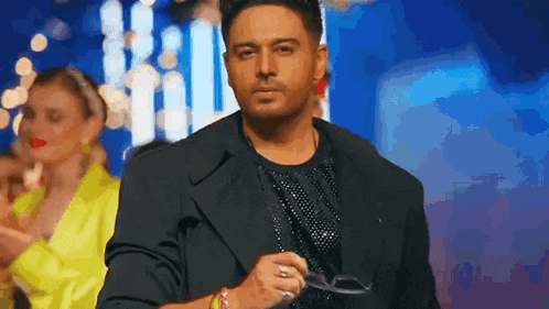 a man in a black suit is walking down a runway holding a pair of glasses .
