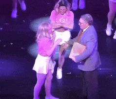 a woman in a pink shirt and white skirt is standing on a stage