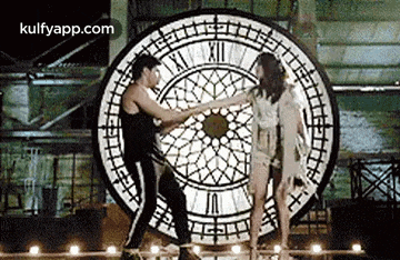 a man and a woman are dancing in front of a giant clock .