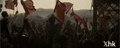 a crowd of people holding up red flags with xhk written on the bottom right