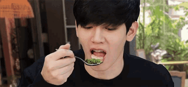 a young man is eating a spoonful of food with his mouth open .