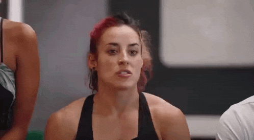 a woman with red hair is making a funny face while standing next to a man in a gym .