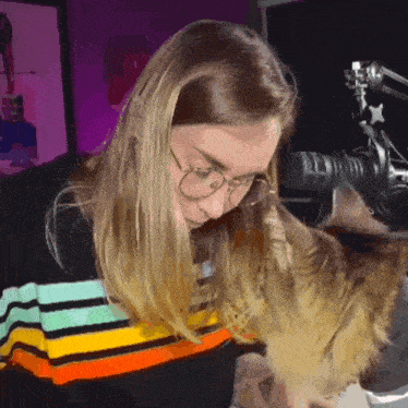 a woman wearing glasses is petting a cat in front of a camera