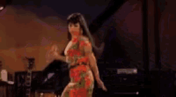 a woman in a floral dress is dancing on a stage in a dark room .