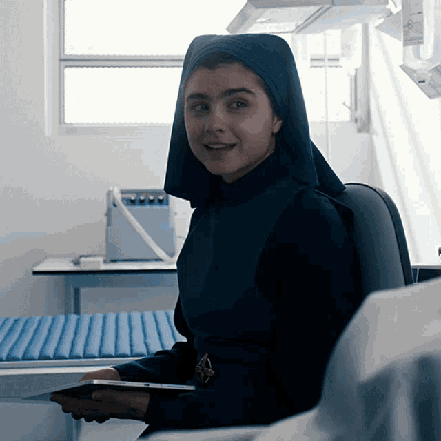 a woman in a nun 's outfit is sitting in a chair holding a tablet