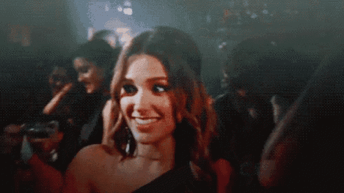 a woman in a black dress is smiling in front of a crowd of people