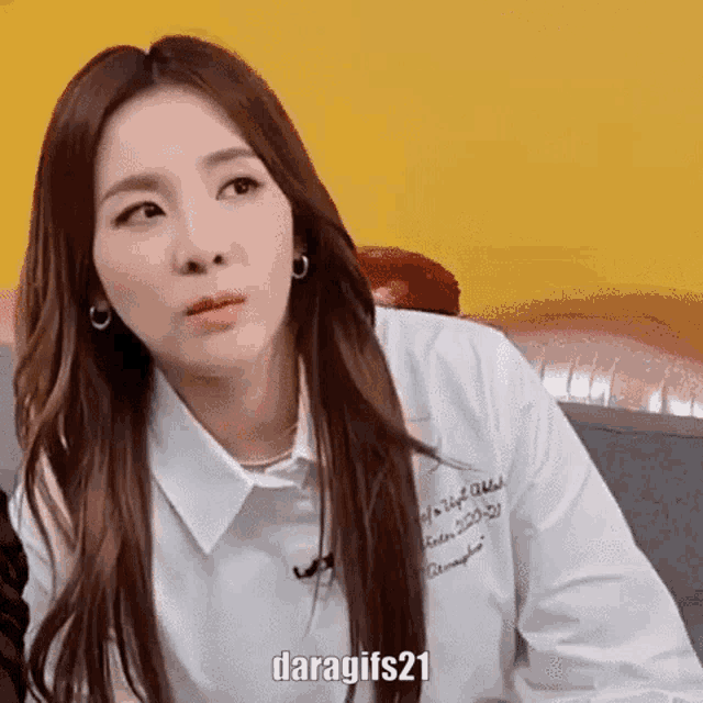 a woman wearing a white shirt and earrings is sitting on a couch and making a funny face .