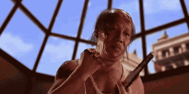 a man with a bloody face is holding a sword in front of a window