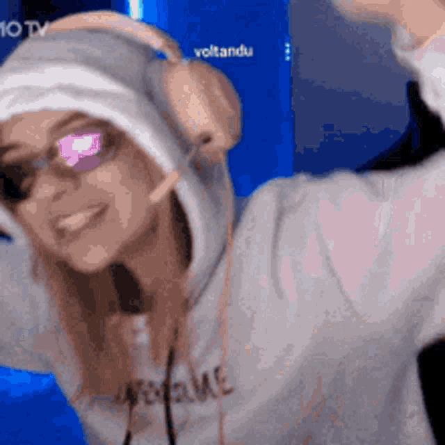 a woman wearing a hoodie and headphones is dancing in front of a blue background .