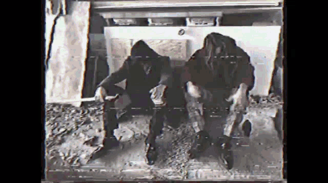 a black and white photo of two men sitting on the ground .
