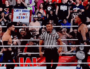 a referee is standing in the middle of a wrestling ring while two wrestlers are fighting in front of a crowd .