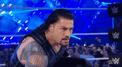 roman reigns is standing in a wrestling ring with a crowd watching .