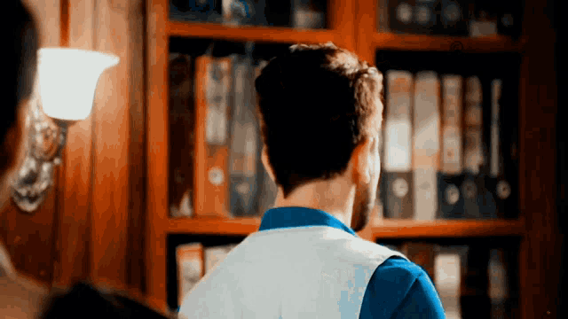 a man in a blue shirt stands in front of a bookshelf full of binders