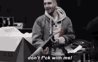 a man in a bomber jacket is standing next to a box and says don 't f * ck with me .