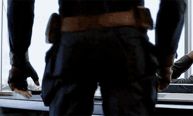 a man in a superhero costume is standing in front of a window with his back to the camera .