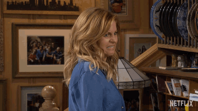 a woman in a blue shirt stands in front of a shelf with netflix written on it