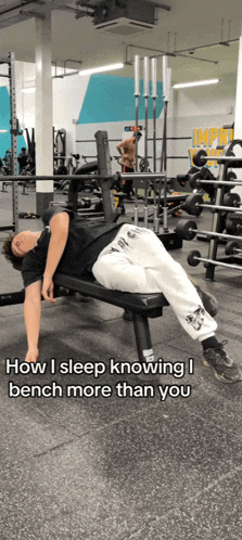 a man is laying on a bench in a gym with a caption that says how i sleep knowing i bench more than you
