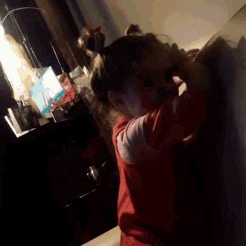 a little girl in a red shirt is looking at something in the dark