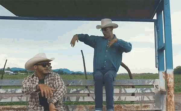 two men wearing cowboy hats are sitting on a wooden bench