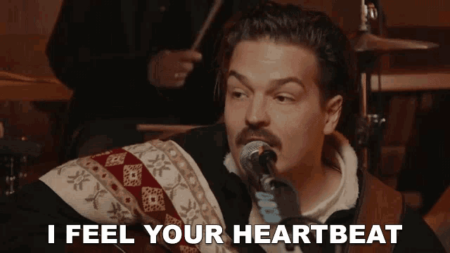 a man singing into a microphone with the words i feel your heartbeat below him