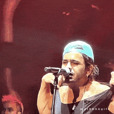 a man wearing a blue hat is singing into a microphone on stage .
