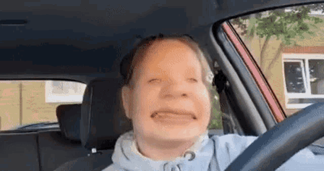 a young girl is driving a red car and making a funny face .