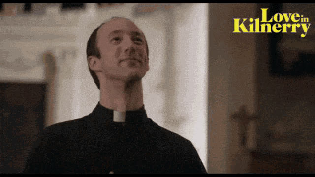 a man in a priest 's collar stands in front of a sign that says love in killarney