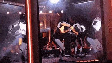 a group of robots are dancing in a room with a sign that says ' clock ' on it