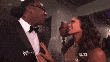 a man in a tuxedo is talking to a woman in a green dress who is wearing a wrestling outfit sponsored by usa