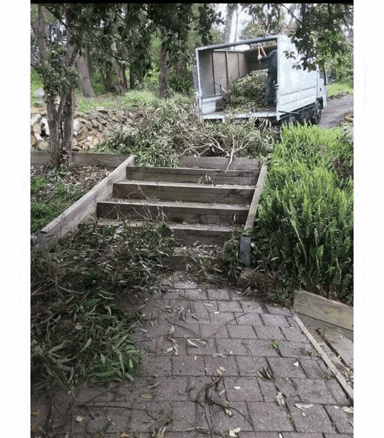 a man is loading branches into a truck on a brick sidewalk .